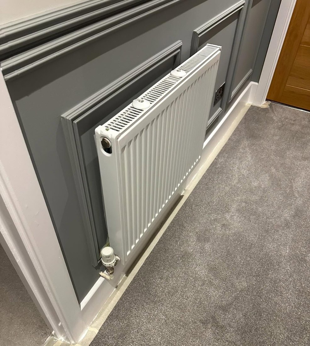 White radiator fitted against a grey panelled wall