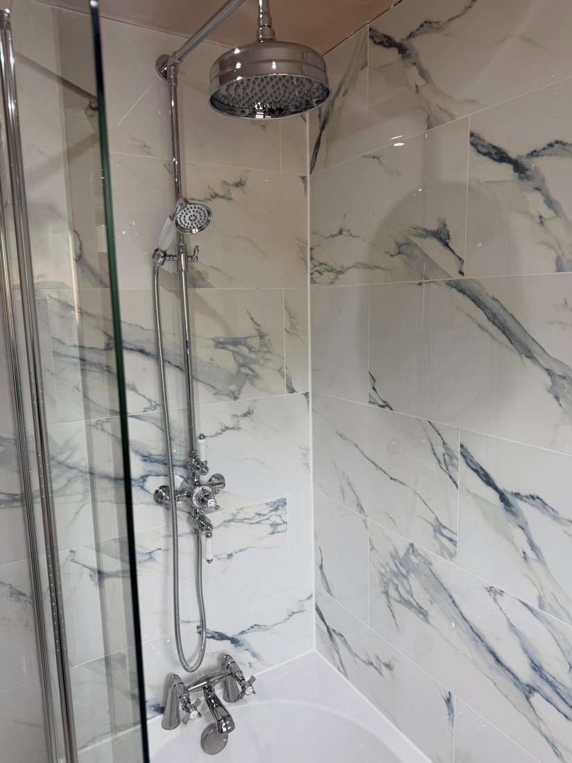 Chrome rainfall and handheld shower on marble-effect tiling